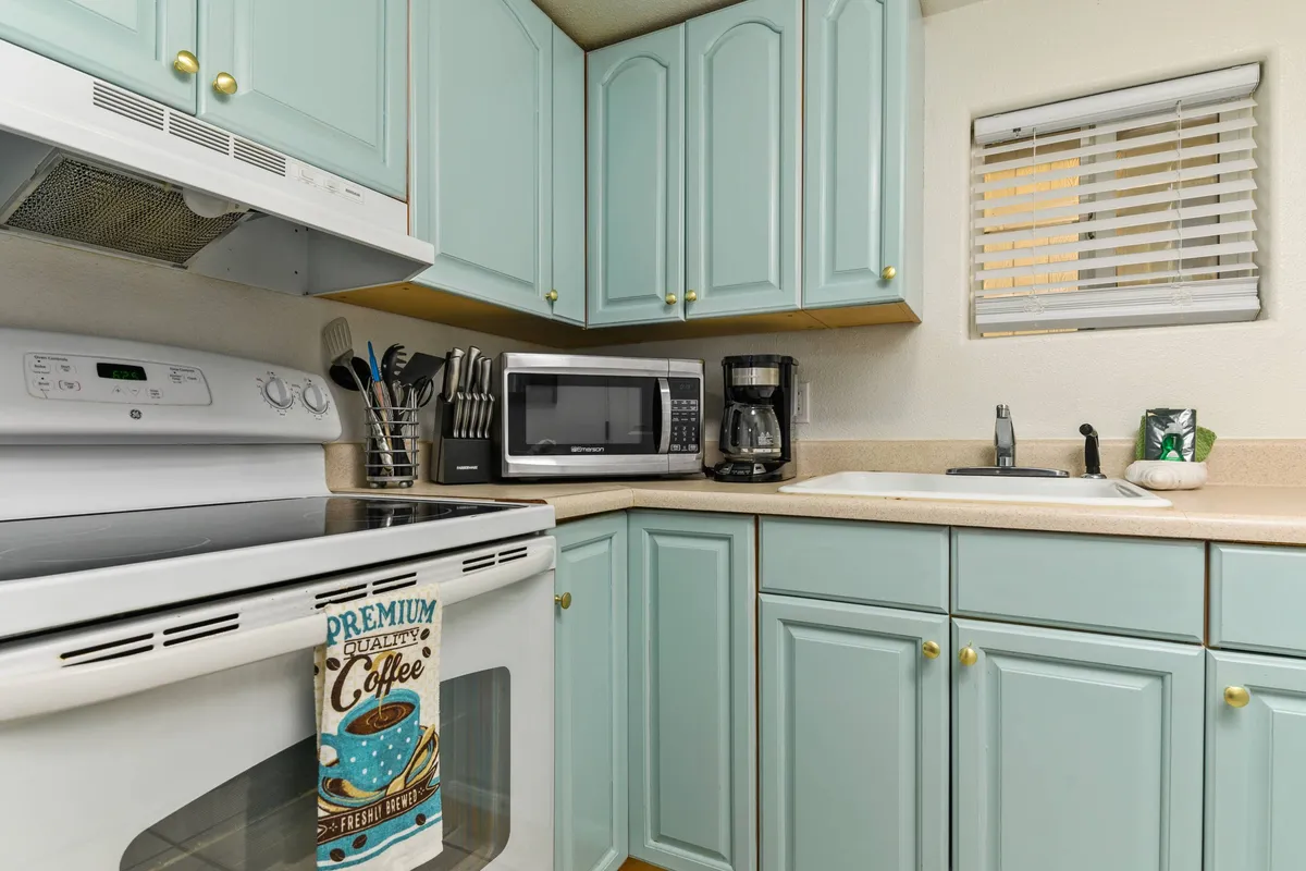 This image highlights a charming kitchen area with light blue cabinets, stainless steel appliances, a coffee maker, and a microwave. The setup suggests a bright, efficient space perfect for preparing meals or enjoying a morning coffee, with a fresh and cheerful color palette that aligns with coastal décor.