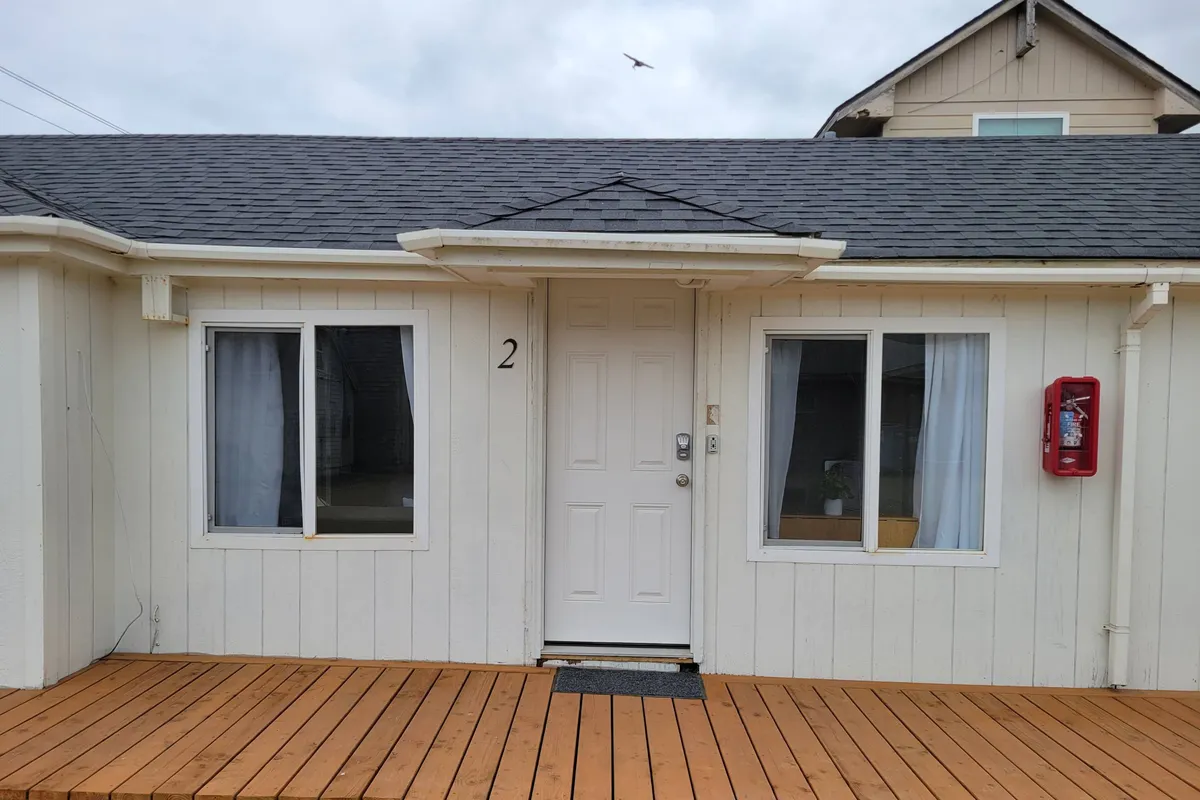 An inviting exterior shot of the motel's front door, large windows, and wooden deck, marked by the number 2. The deck looks like an ideal spot for relaxing or letting pets bask in the sun after a day’s walk.
