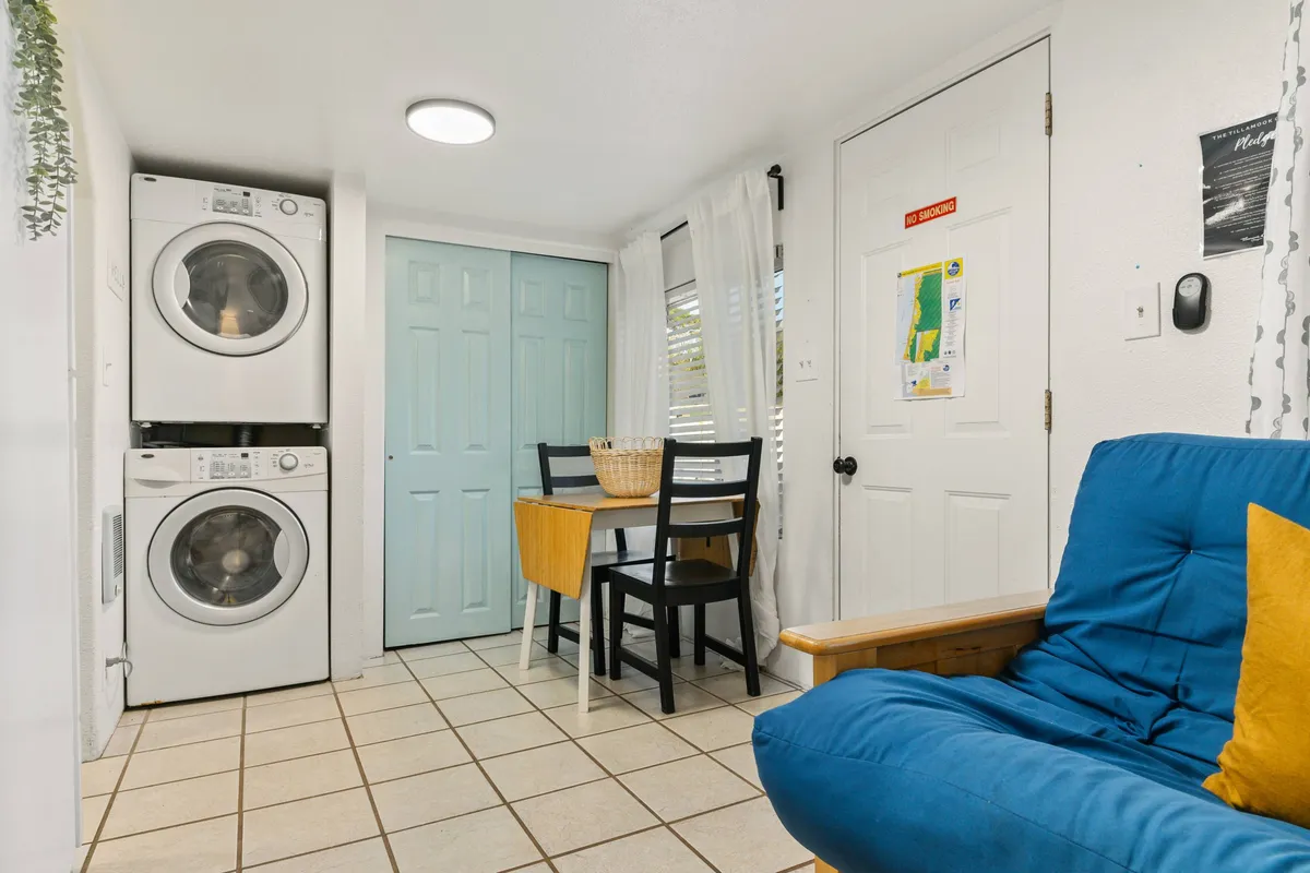 This inviting scene features a small dining table positioned near a blue futon and a stacked washer and dryer. The multifunctional area reflects a practical yet cozy setting, perfect for casual meals, relaxation, and accommodating additional guests with the futon.