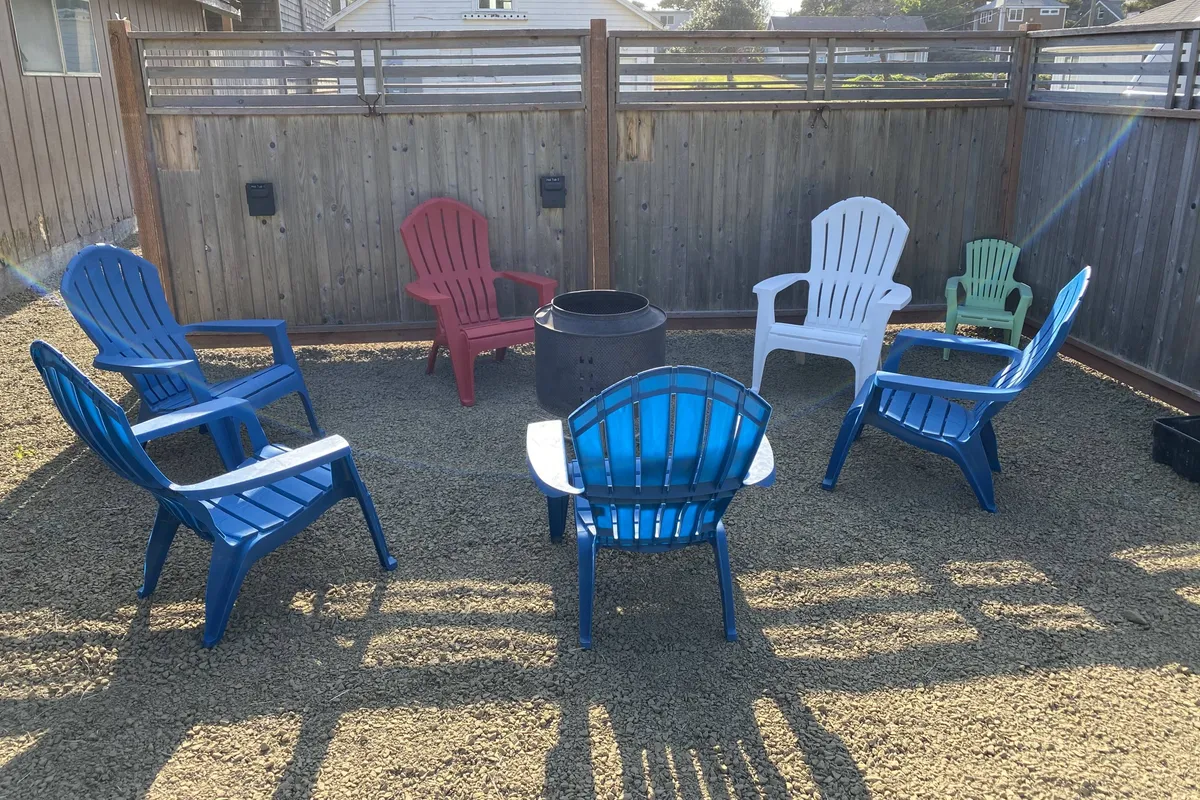A cozy fire-pit area surrounded by colorful chairs, with guests gathered and engaged in lively conversations. The warm glow from the fire creates an inviting atmosphere, perfect for socializing and relaxing in the company of others. The setting is casual and communal, emphasizing the welcoming spirit of the shared outdoor space.